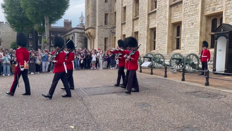 red coat guards march off in line, rifles gleam, their steps in time