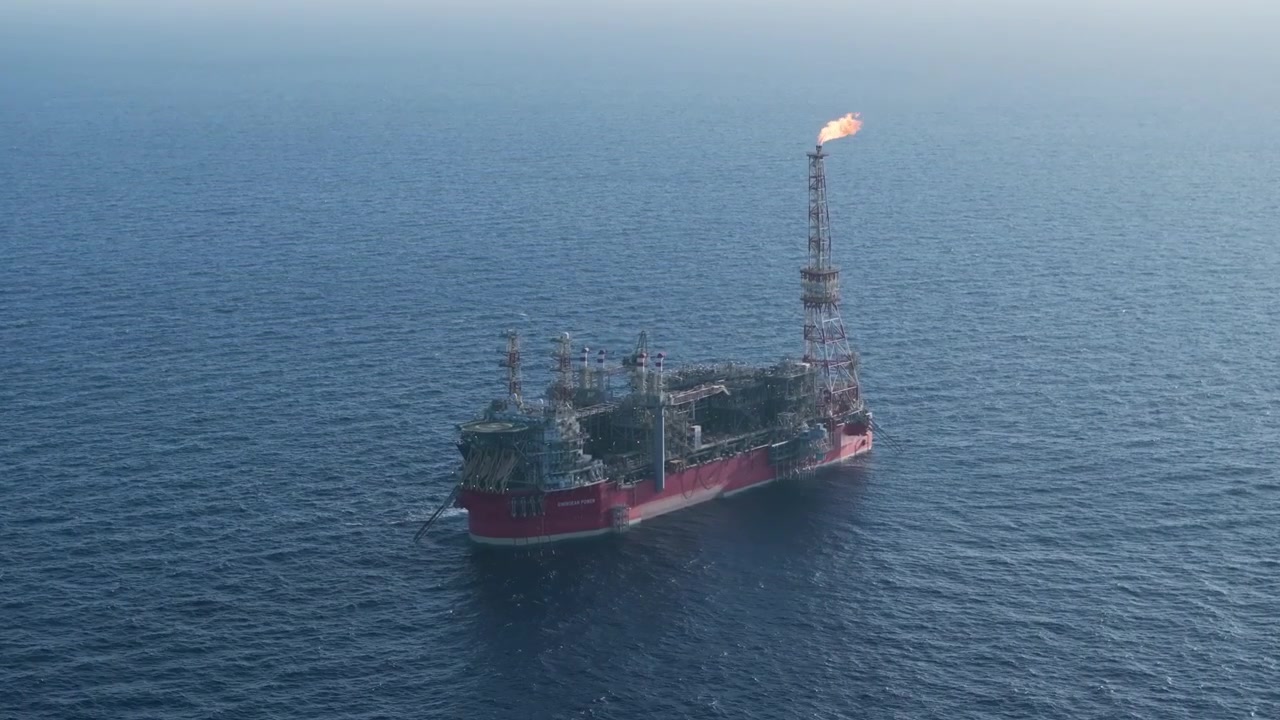Luftfoto af et FPSO-skib (flydende produktions-, lager- og aflæsningsskib) i drift til søs med en klar orange flamme, der brænder fra gastårnet.