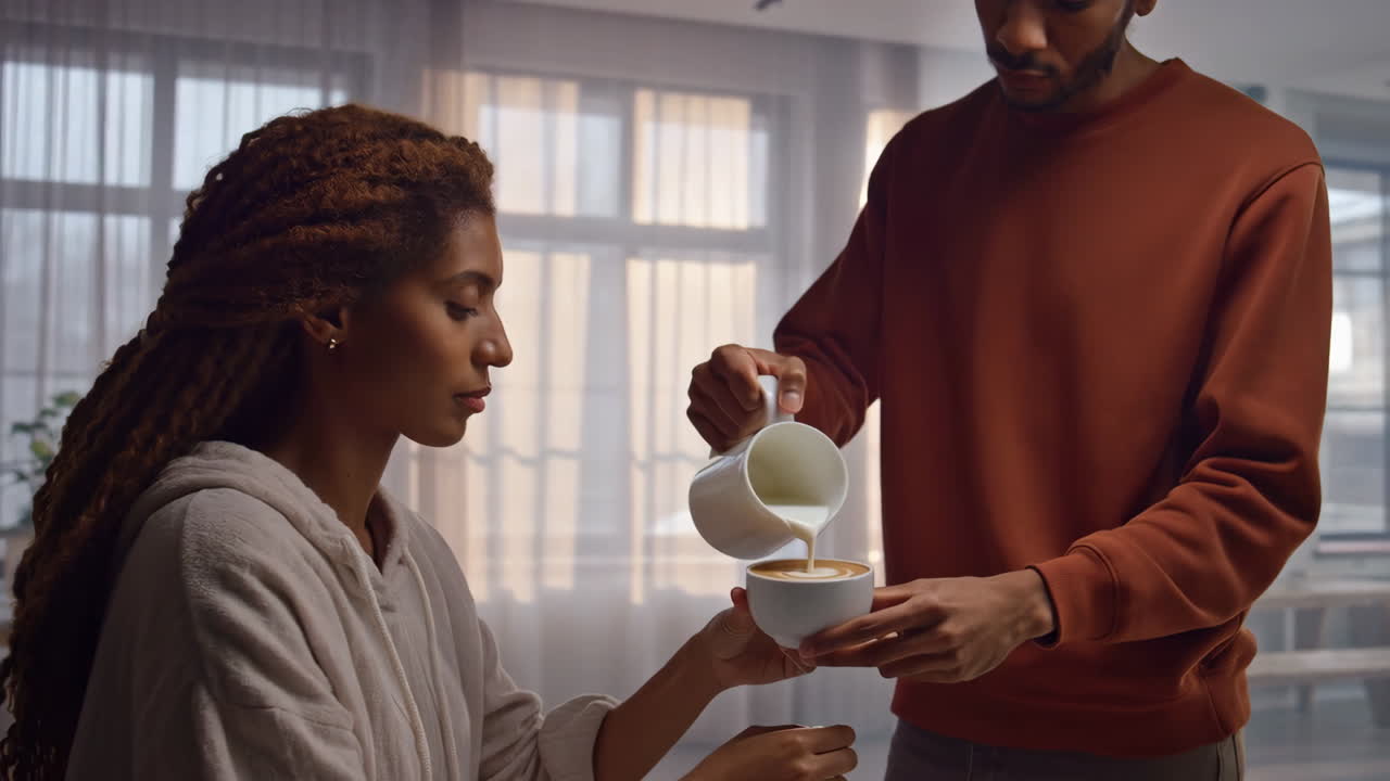 A man pours milk into a woman's coffee cup, making latte art