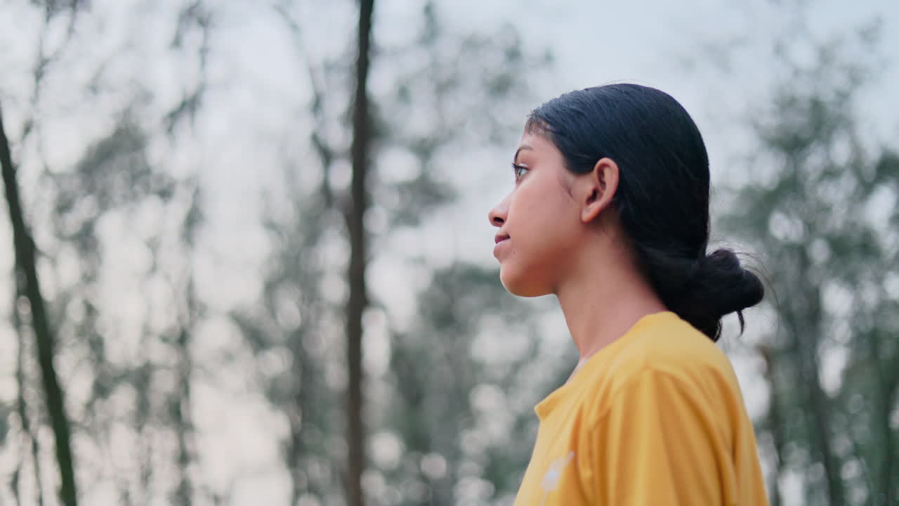 Medium shot of a young woman is looking around and enjoying the nature in the forest in early morning