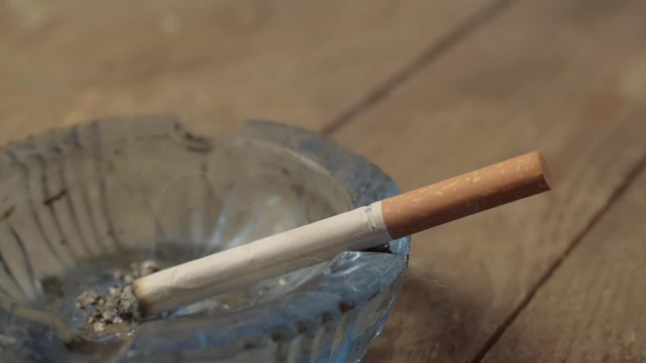 Smoker flicking ash off a burning cigarette into an ashtray