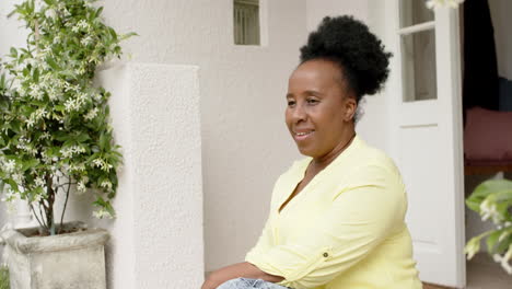 happy african american senior woman sitting and smiling outside house, slow motion