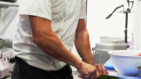 Gimbal-down-revealing-chef-man-chopping-green-herbs-on-a-board-in-slow-motion-with-a-knife