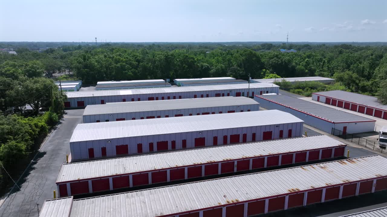Green Self Storage Unit Buildings or Warehouse Temporary Storage at sunny day in Florida. Aerial approaching shot. American suburb garage with forest trees in background.
