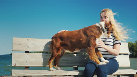 young woman playing with a dog sits on a bench near the sea the wind plays with her hair