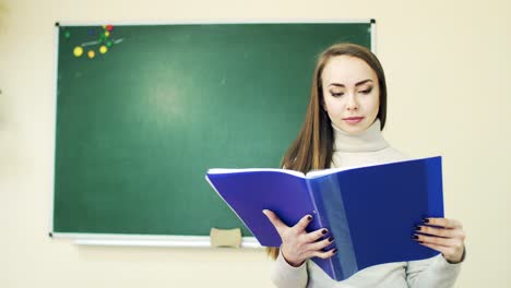 student leafing through notebook in classroom against green school blackboard