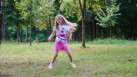 happy girl in pink shorts dancing in the park. full length portrait of a girl jumping on the natural green scenery in summer. slow motion.
