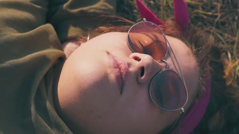 una mujer joven con gafas de sol naranjas duerme en un prado marrón