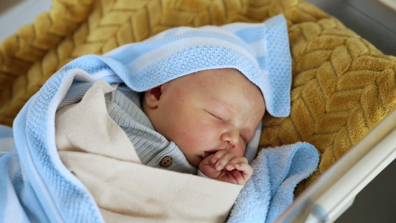 Adorable baby sleeping peacefully in the crib. Newborn child in blankets sleeps holding hand at his mouth. Top view close up.