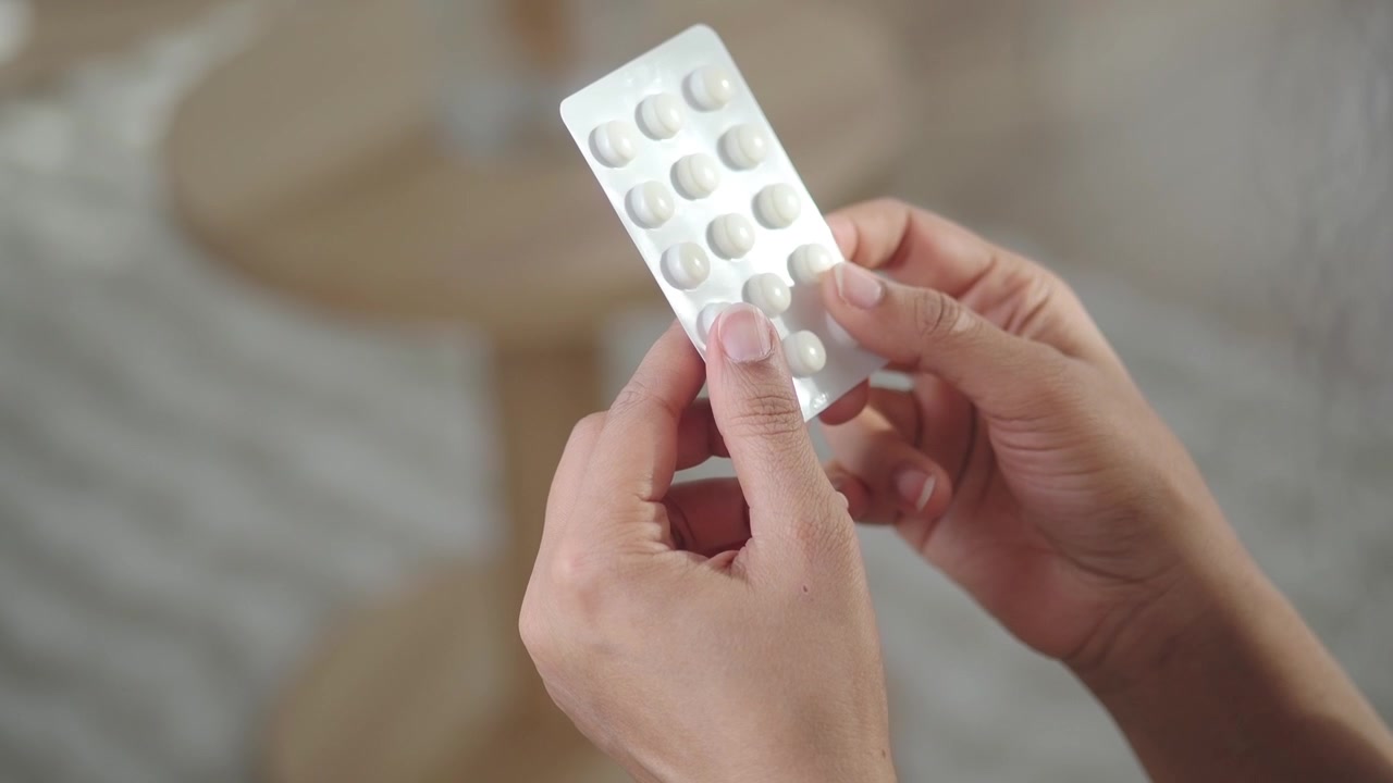 Primo piano di mani che reggono un blister di pillole bianche