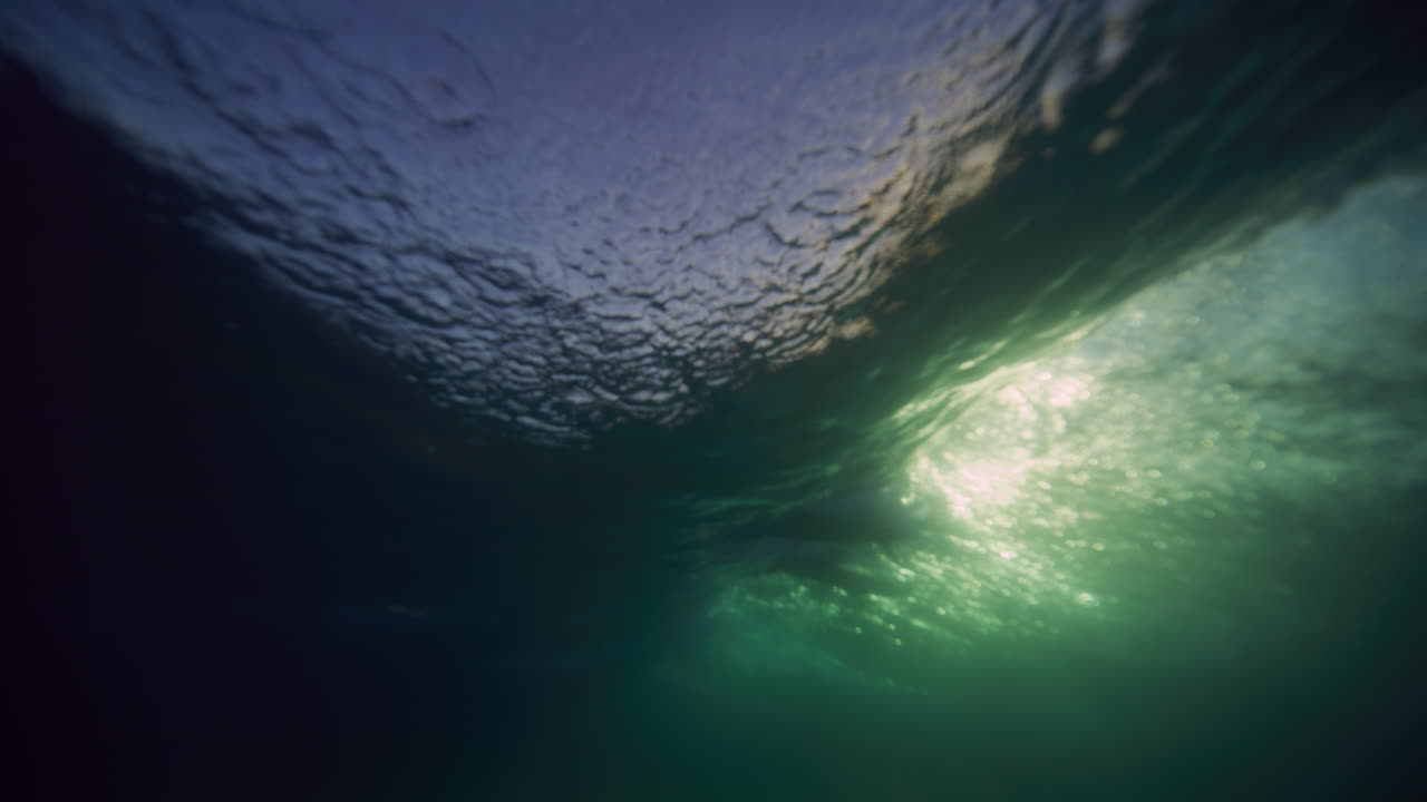 vista submarina de las olas que se rompen brillando con la luz del sol y el surfista