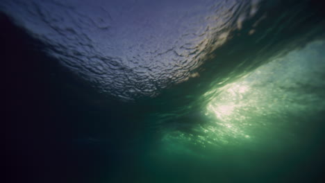vista submarina de las olas que se rompen brillando con la luz del sol y el surfista