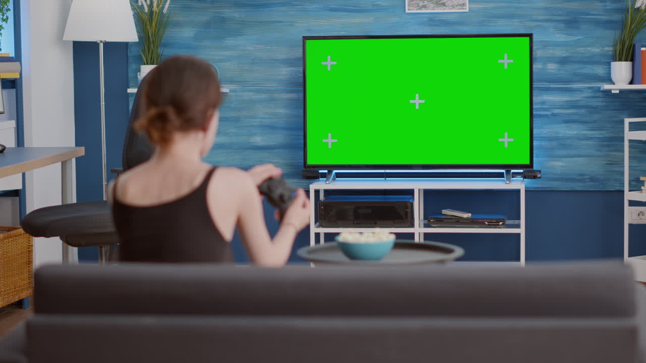 Young woman holding wireless controller playing action console video game on green screen tv