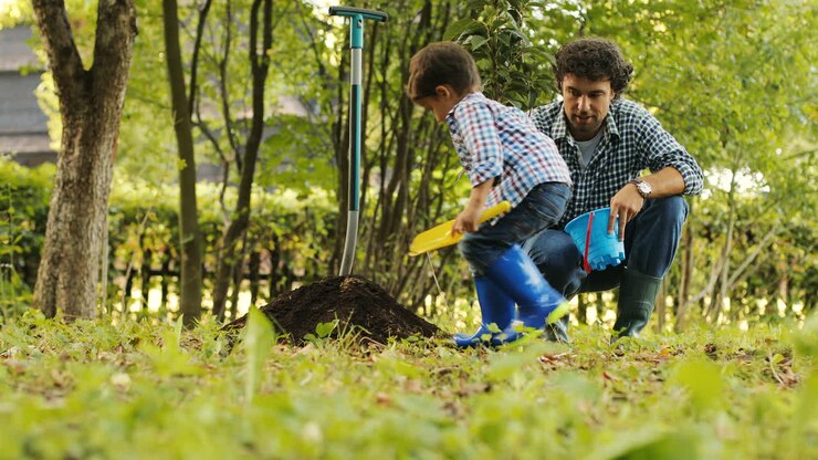 Portrait of a little boy and his dad planting a tree. The boy touches the tree and plays around. Dad takes care of him. Blurred background