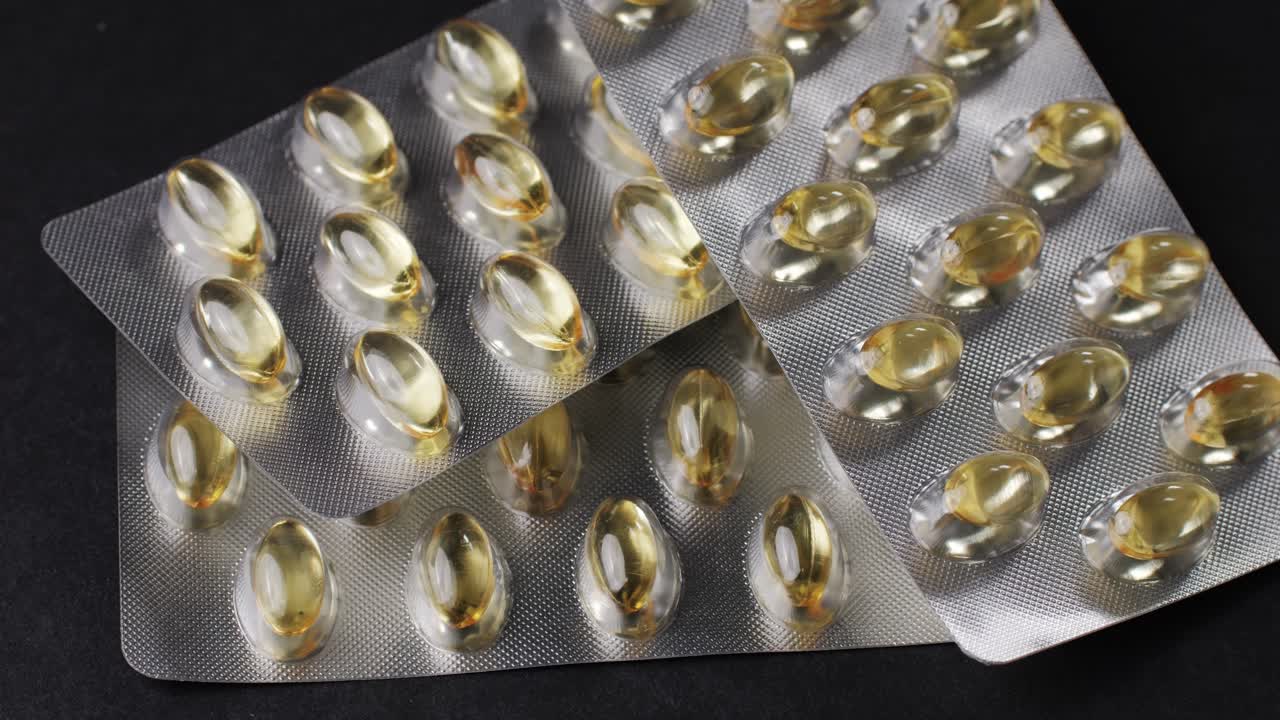 Wrapped omega fish oil gel capsules on black background close-up . Omega vitamins pills 3 6 9. To be healthy and take care of your health. Pharmaceutical industry. Business of biological supplements and vitamin. Pharmacy store delivery
