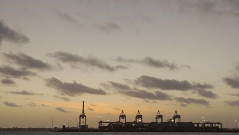 tilting shot of shipping yard in the distance at sunset with wooden pylons in the foreground