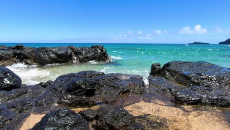 Small-Pacific-Ocean-waves-lap-against-rocky-shoreline-on-Hawaiian-beach