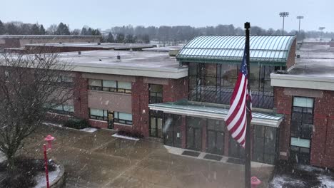 bandera estadounidense ondeando frente a la escuela secundaria durante la tormenta de nieve