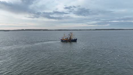 Panning-drone-shot-of-a-Fishers-boat-dragging-the-nets-thru-the-water-of-the-shore-of-Ameland