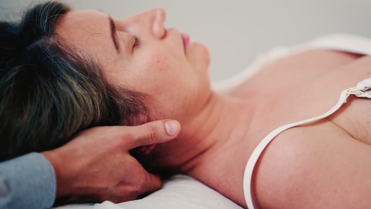 Profilo laterale di una donna sdraiata su un lettino per trattamenti mentre un terapista le sostiene il collo e la testa durante una sessione rilassante di terapia manuale