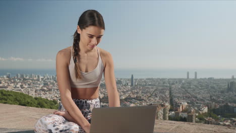 Mujer-Sentada-En-Pose-De-Loto-Con-Una-Computadora-Portátil-Al-Aire-Libre.-Chica-Escribiendo-En-La-Computadora-Portátil-En-La-Ciudad