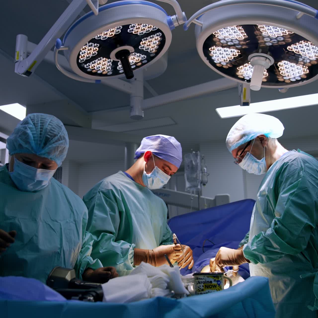 Two male medics cooperate performing surgery on foot. Female nurse arranges tool and devices on the instrument stand