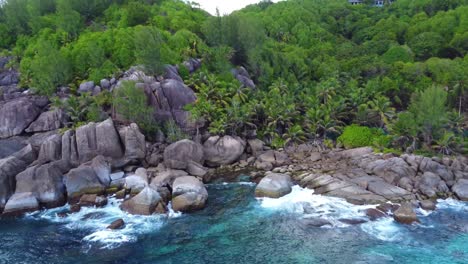 palm trees and waves crashing into granite boulder on the coast of the seychelles