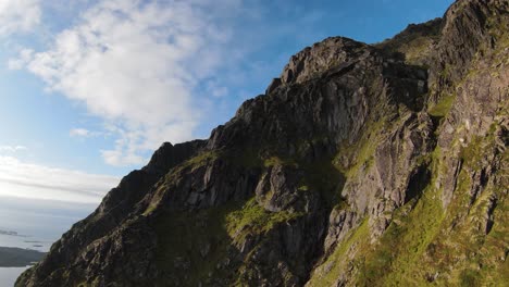 Flying-along-a-mountain-overlooking-a-lake-and-grassy-landscape-and-many-trees-on-the-hillside,-in-slowmotion