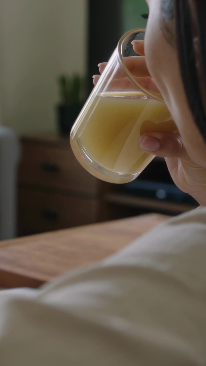 Video vertical: Mujer levantando un vaso, bebiendo jugo en la sala de estar, espacio para texto