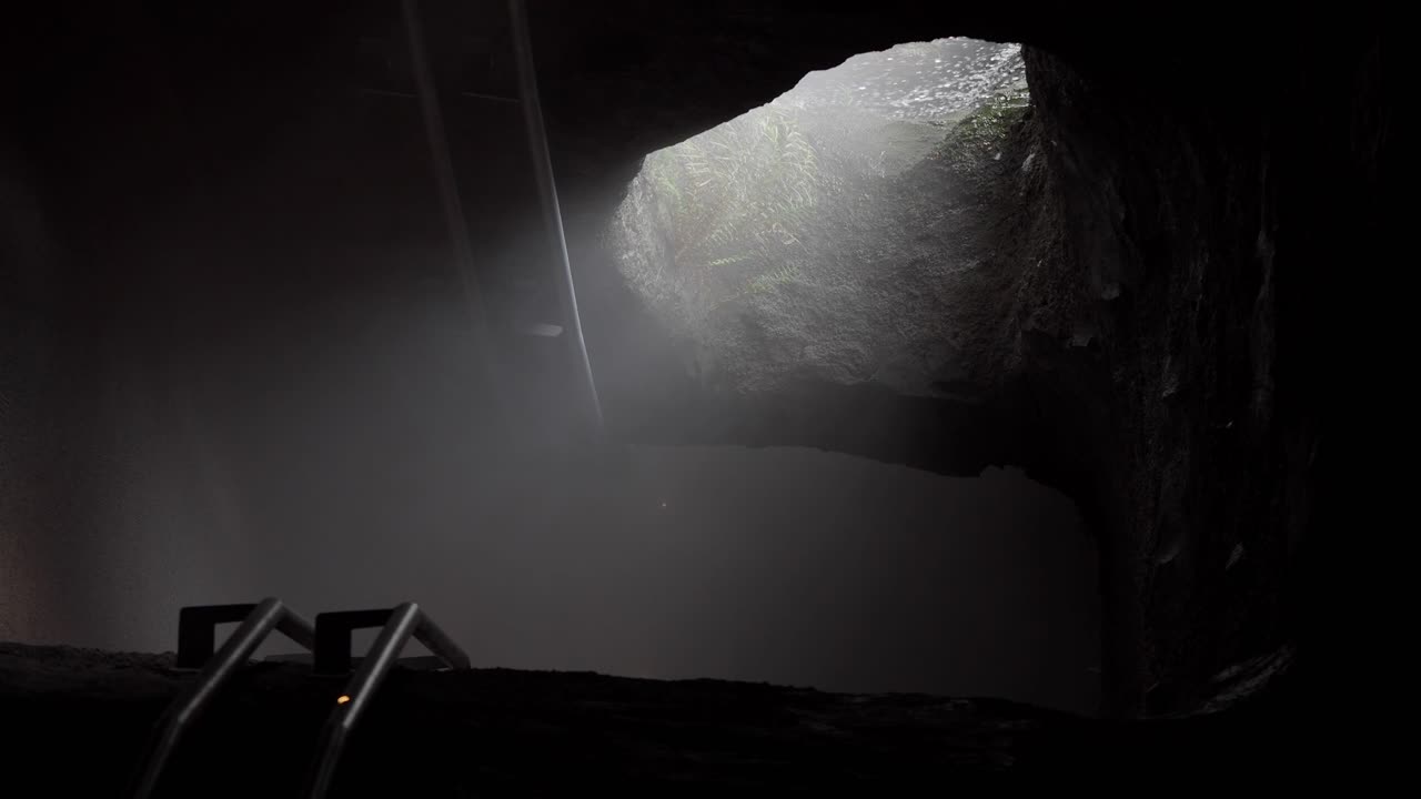Inside a dark cave with a ladder leading to a hole with light