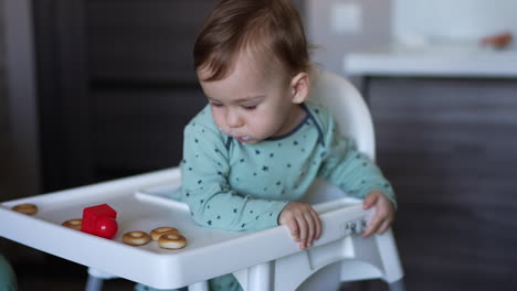 nourishing baby boy sitting in the chair. mom is shoving the full spoon to a boy but he is distracted by something else and turned away.
