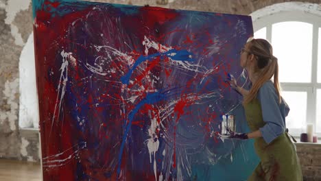 woman works on abstract painting, sprinkles paints on canvas emotionally