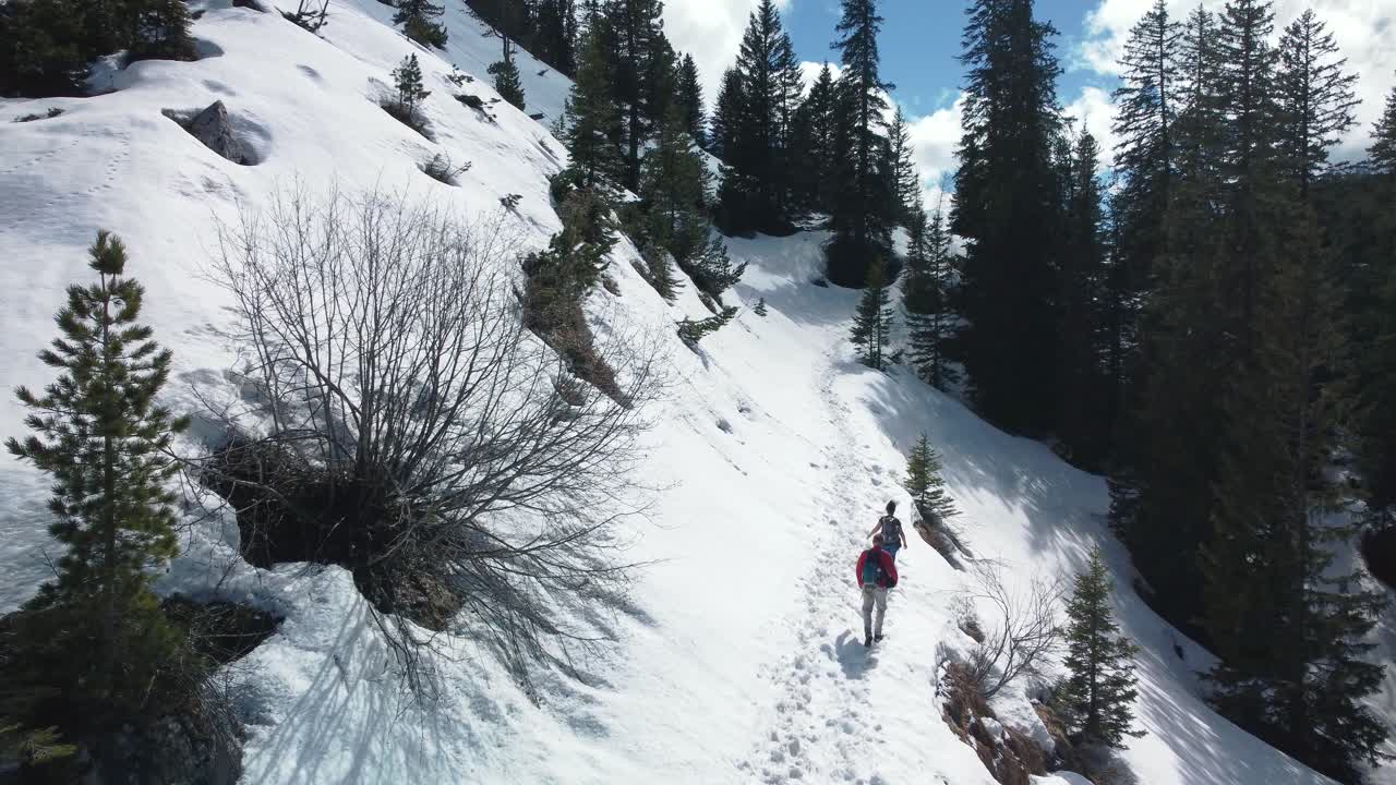 dos personas, un hombre y una mujer, caminan en un épico camino panorámico de montaña nevada muy por encima del pintoresco castillo de elmau de baviera y picos glaciares en los alpes bávaros austríacos en un día nublado y soleado en la naturaleza