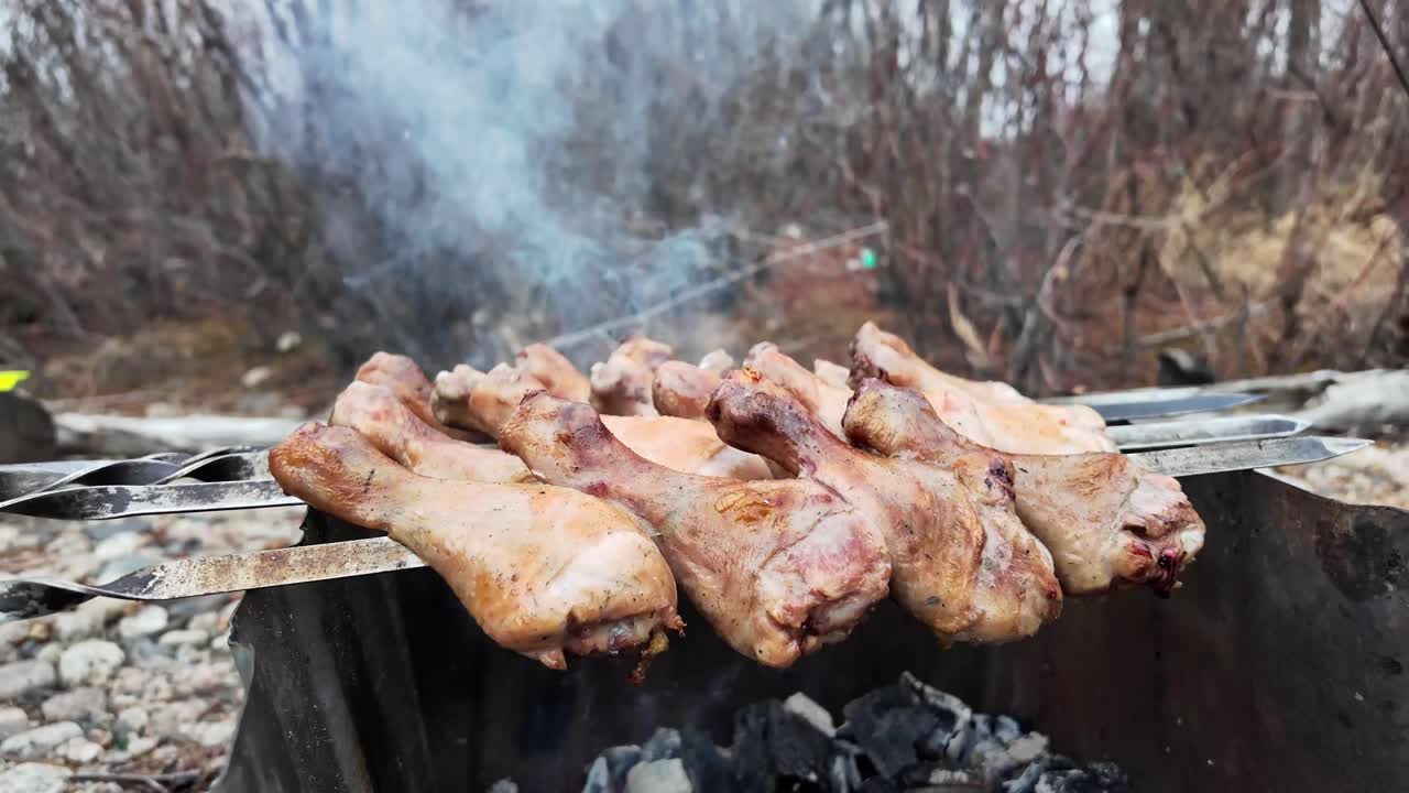 Cooking chicken legs on skewers on hot coals in the forest in spring