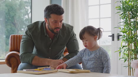 padre con síndrome de down hija jugando un juego con una carta de madera en casa juntos