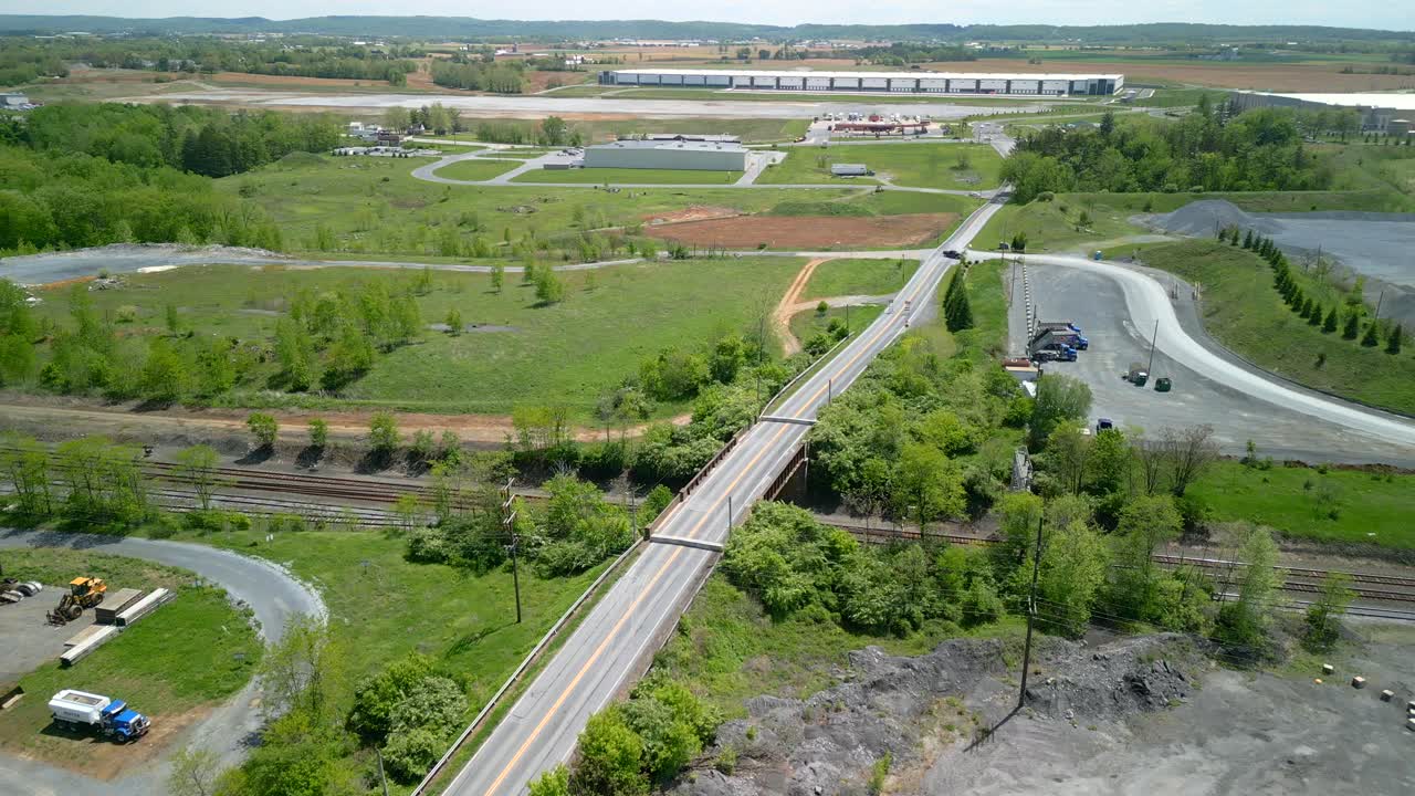 Aerial drone video of a bridge under construction with signs and pillars. Green grass fields and blue skies during the daytime.
