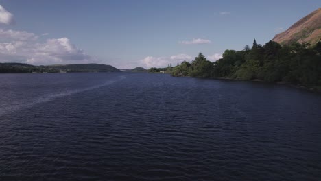 Low-drone-shot-flying-forward-along-a-lake-shoreline-on-a-sunny-day,-Ullswater,-Lake-District,-Cumbria,-UK