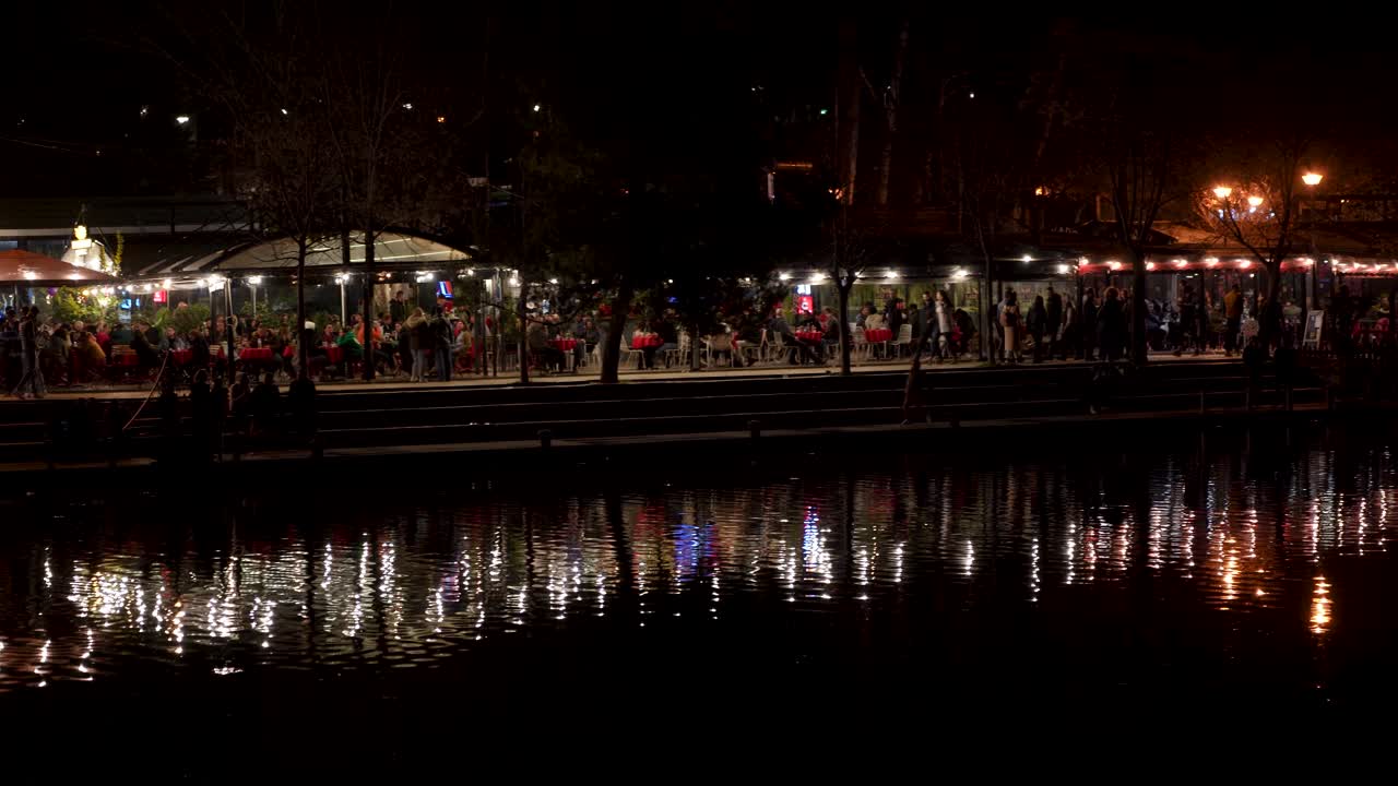 bar nocturno escénico junto al lago: gente disfrutando de bebidas con reflejos de luces en el agua
