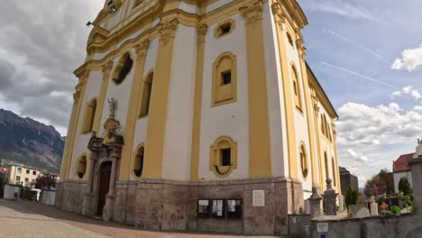 wide angle view of the yellow and white baroque pfarrkirche und basilika mariae empfängnis in innsbruck, austria, showcasing its elegant architecture, stone base, and alpine backdrop, tilt up camera