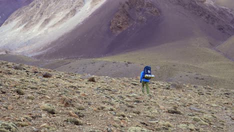 trekking in the andes mountains. mendoza province, argentina. zoom in view of a man with a backpack exploring a desolate and arid landscape.