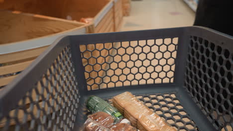 a lady in a black coat and black boots placing a loaf of bread into a shopping trolley that already contains a pack of biscuits and a little juice