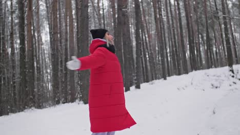 una joven alegre disfrutando del invierno en el bosque. una mujer con un abrigo rojo girando.
