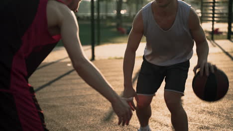 Primer-Plano-De-Un-Hábil-Jugador-De-Baloncesto-Botando-El-Balón-Entre-Las-Piernas,-Mientras-Que-Un-Segundo-Jugador-Defiende-En-Una-Cancha-De-Baloncesto-Al-Aire-Libre