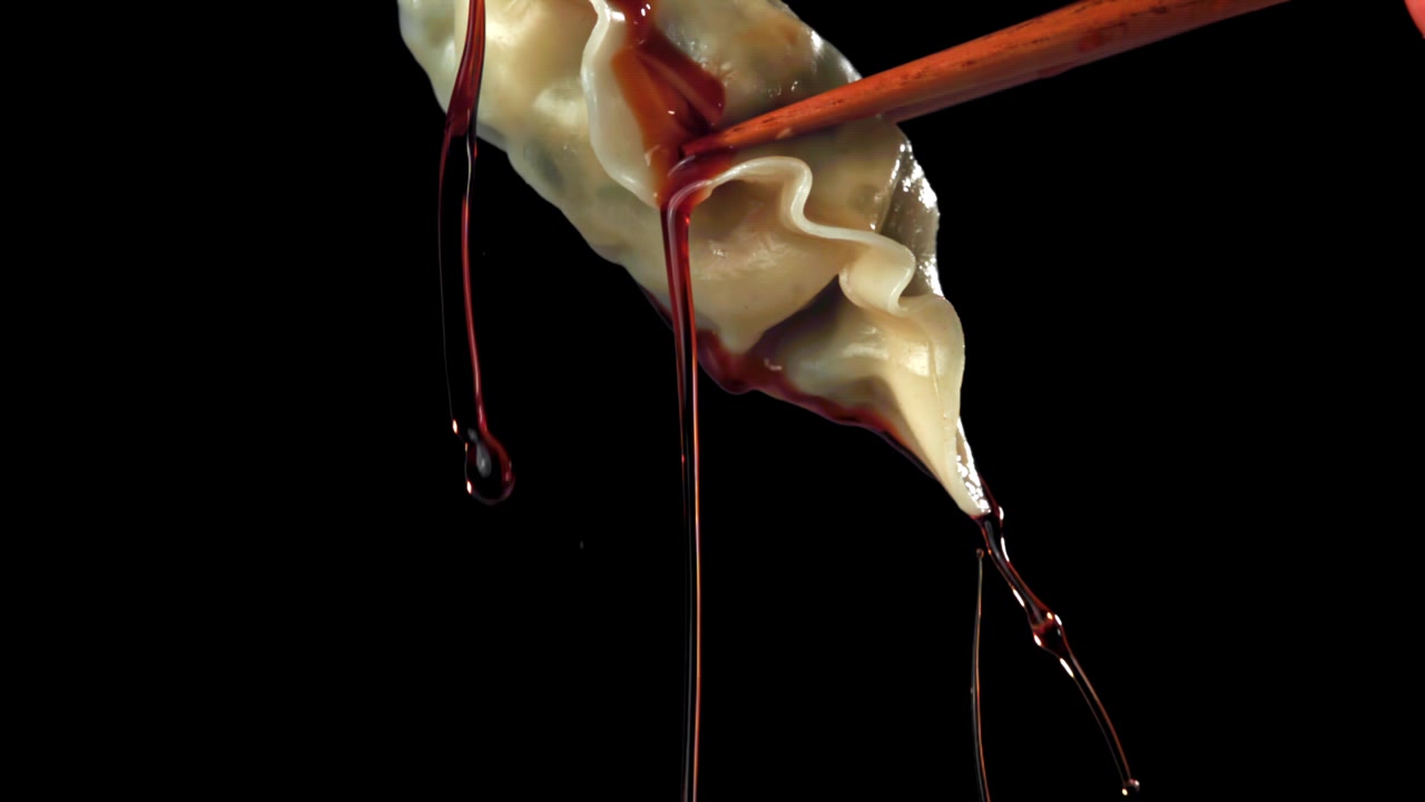 Salsa rossa che cola da un raviolo tenuto con le bacchette, al rallentatore