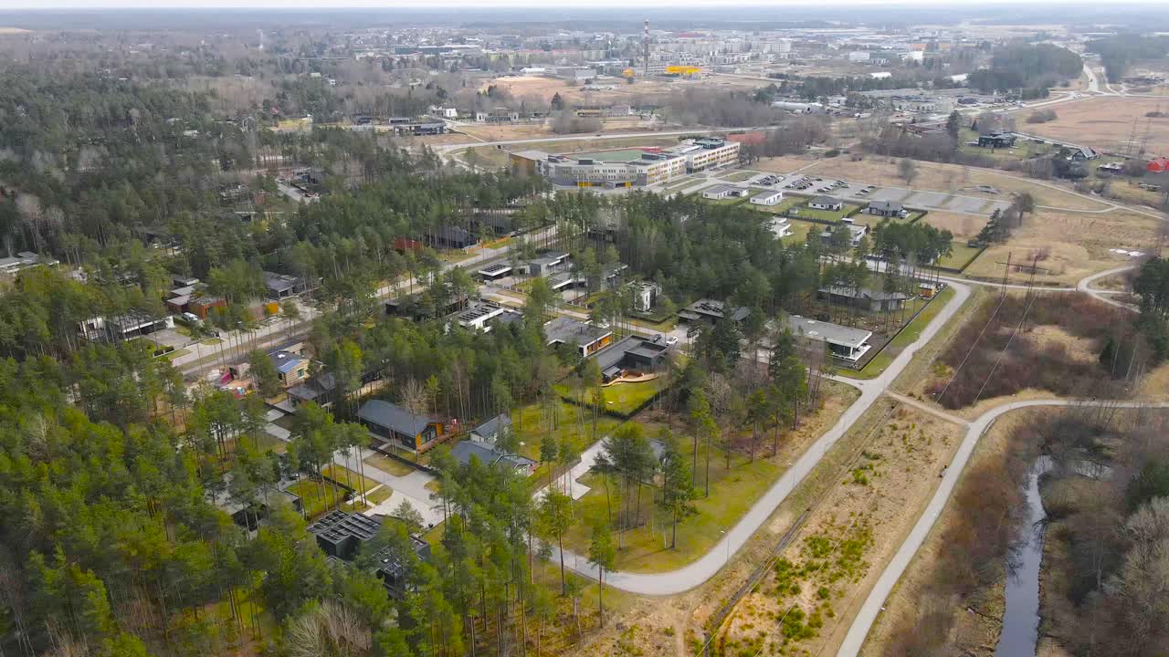 Aerial drone footage showing a peaceful and beautiful living neighborhood in Saue Estonia Laagri during a sunny spring day. Small houses and rooftops are visible between roads and tall pine trees.
