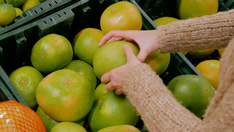 Woman buying fresh exotic citrus fruits at grocery store