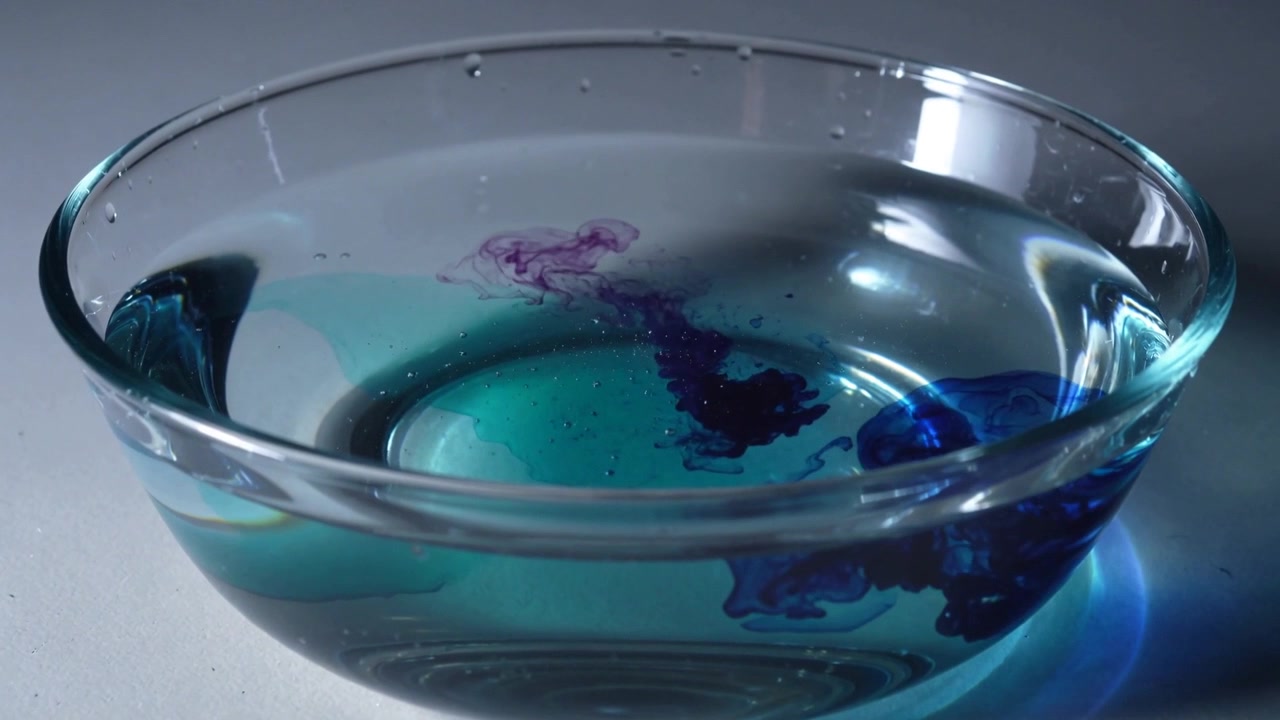 Appearing purple droplet, sinking in bowl water on tabletop in studio, merging to mix blue dye