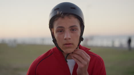 close up portrait confident teenage boy takes off helmet smiling enjoying relaxed summer vacation on seaside park at sunset slow motion