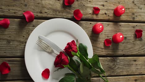 candles and red roses on plate on wooden background at valentine's day