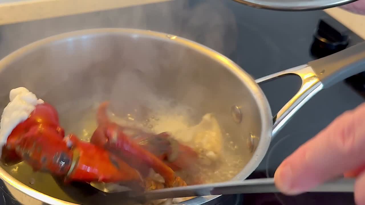 Close-up of lobster claws being stirred in a boiling pot on a stove.